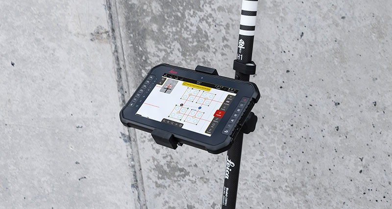 Software Leica iCON trades para replanteo en una tableta negra fijada a un Leica iCON vPole delante de una pared de cemento.